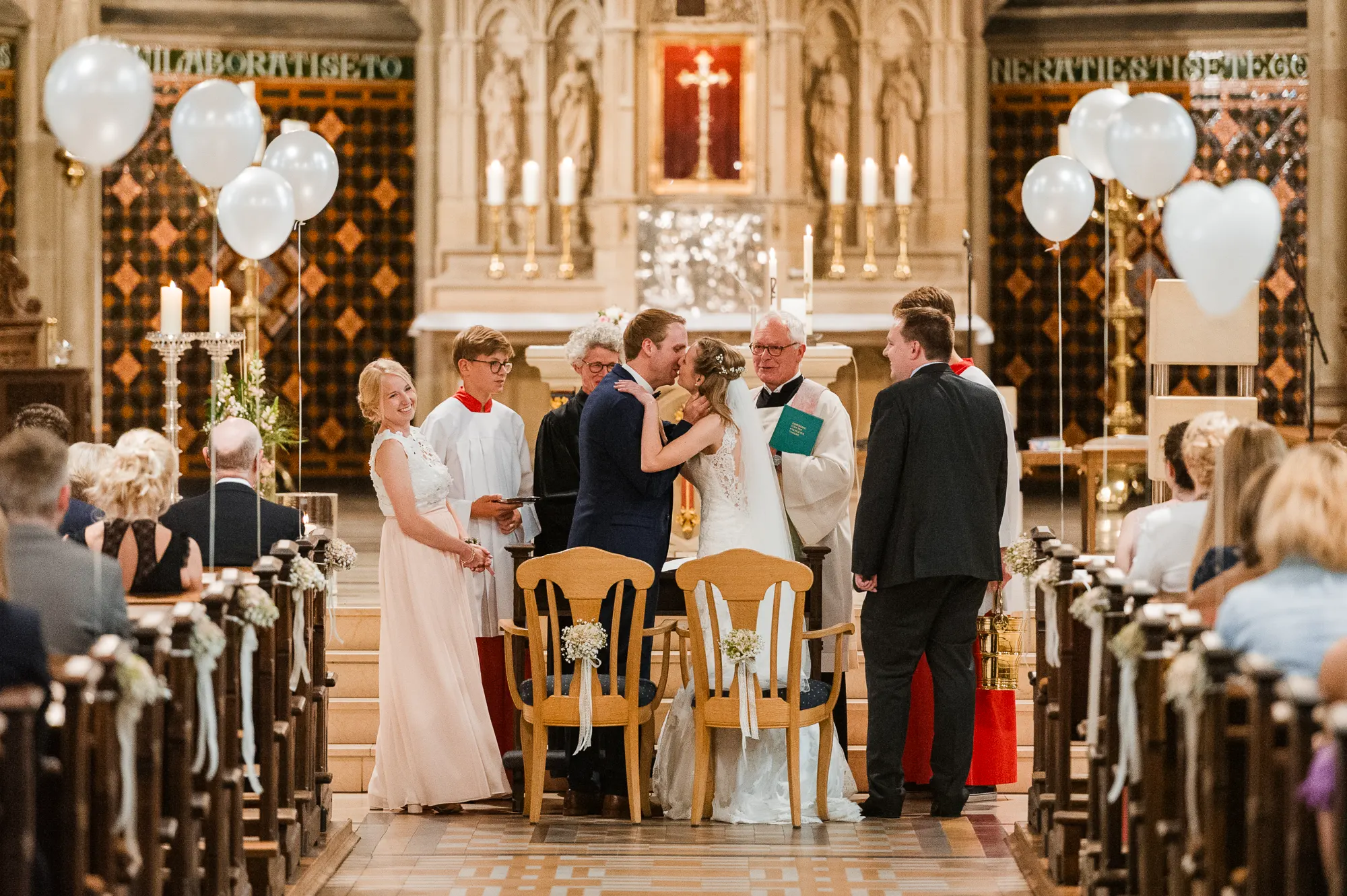 Brautpaar küsst sich nach dem Ja-Wort und dem Ringwechsel in der St. Lamberti Kirche in Ochtrup, umgeben von Hochzeitsgästen und weißen Luftballons