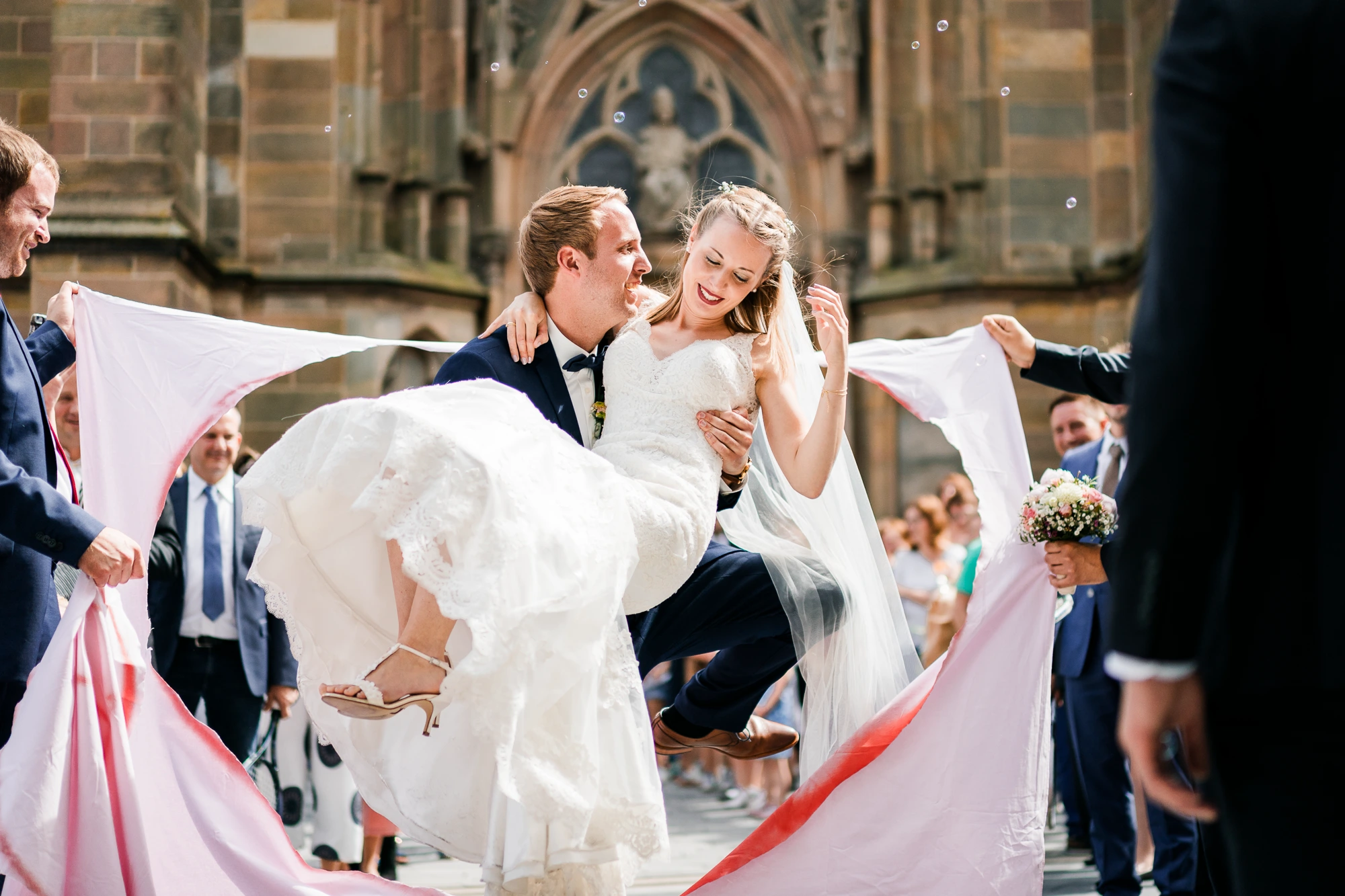 Bräutigam trägt die Braut durch ein aufgeschnittenes Herz auf einem Laken vor der St. Lamberti Kirche in Ochtrup
