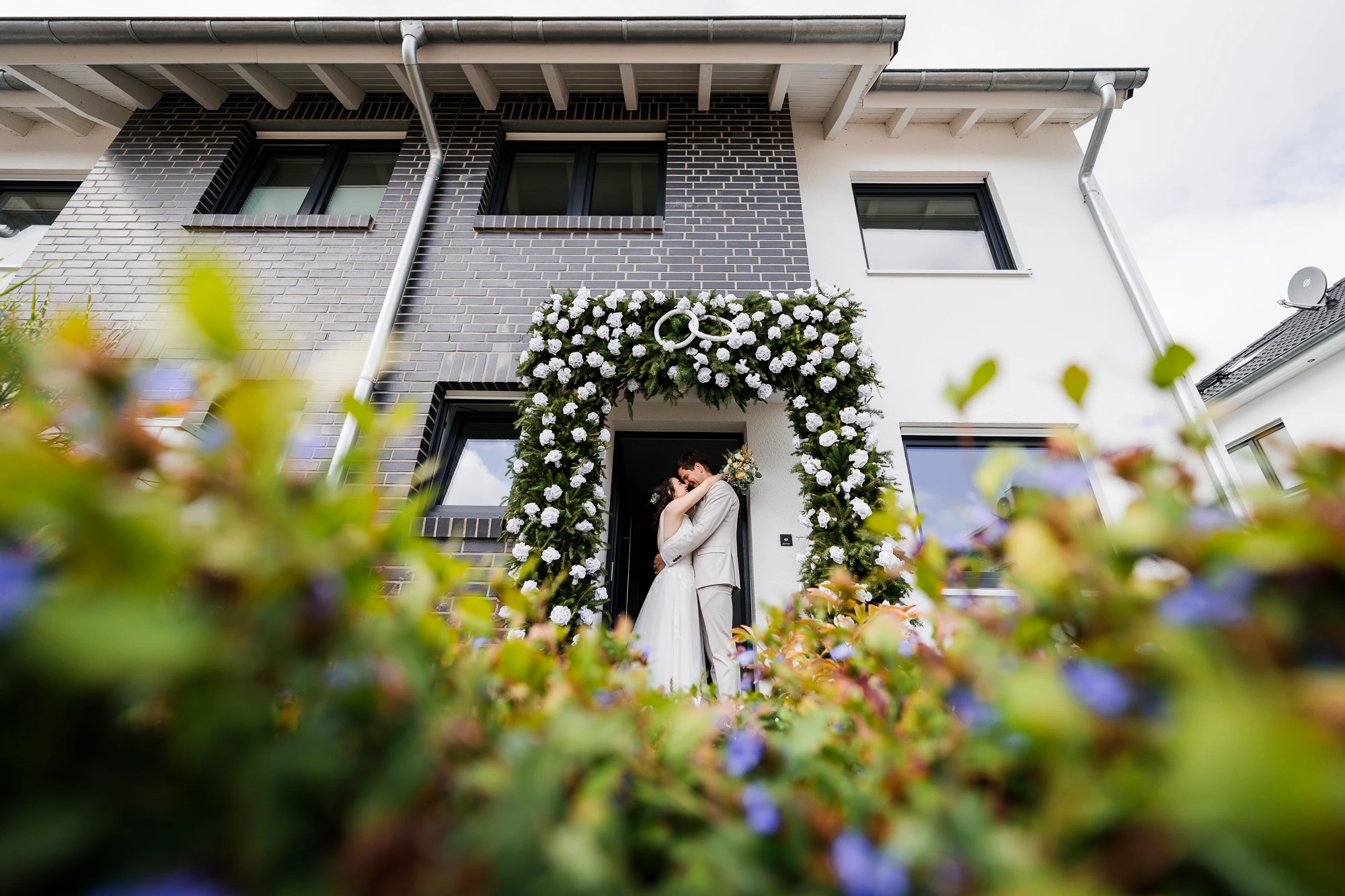 Brautpaar küsst sich nach dem Ersten Sehen am Hochzeitstag unter einem Bogen an der Haustür ihres Zuhauses in Ochtrup - Hochzeitsfotograf Ochtrup