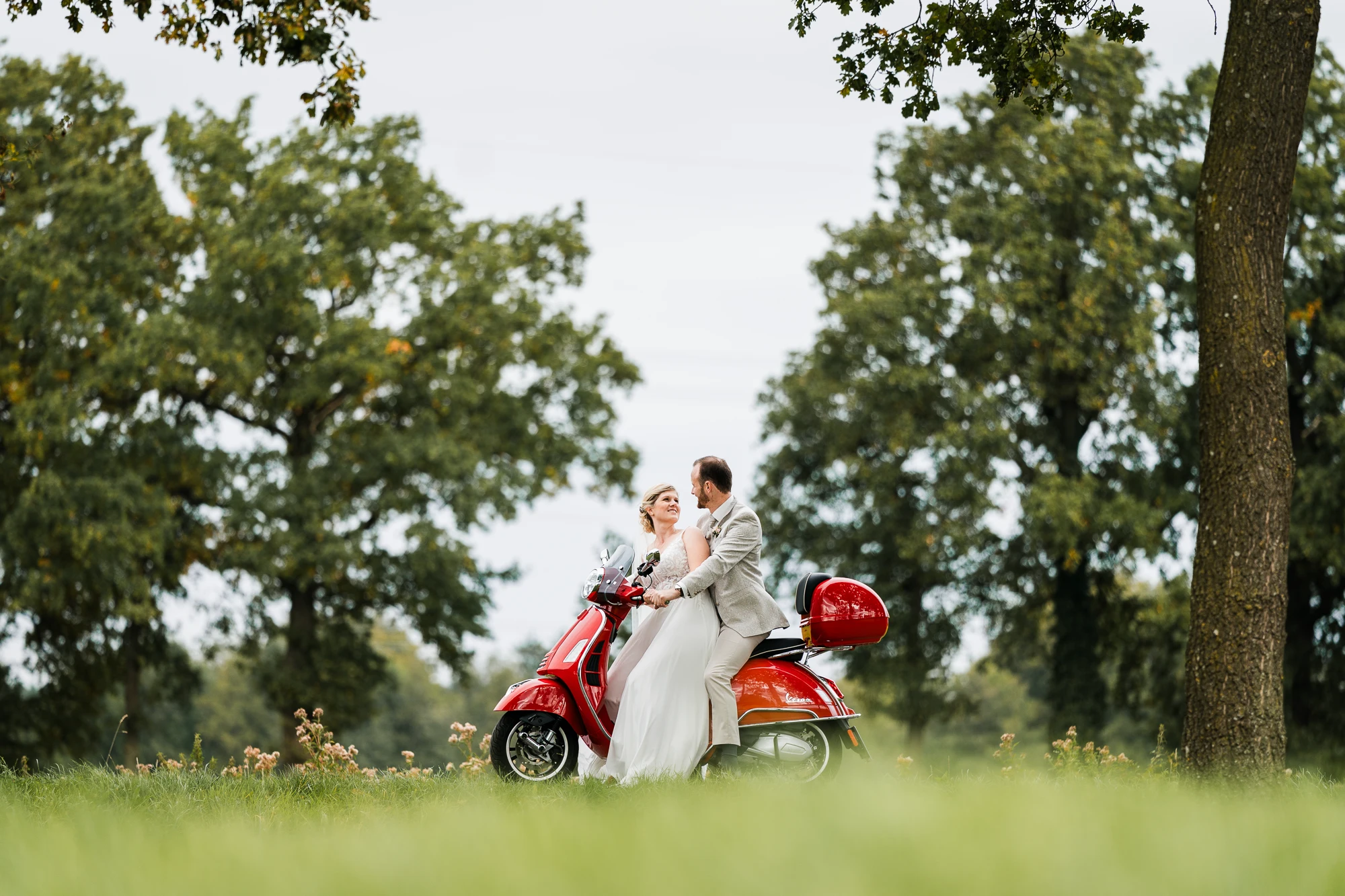 Brautpaar an einer roten Vespa inmitten der grünen Münsterländer Landschaft – Hochzeitsfotografie Ochtrup