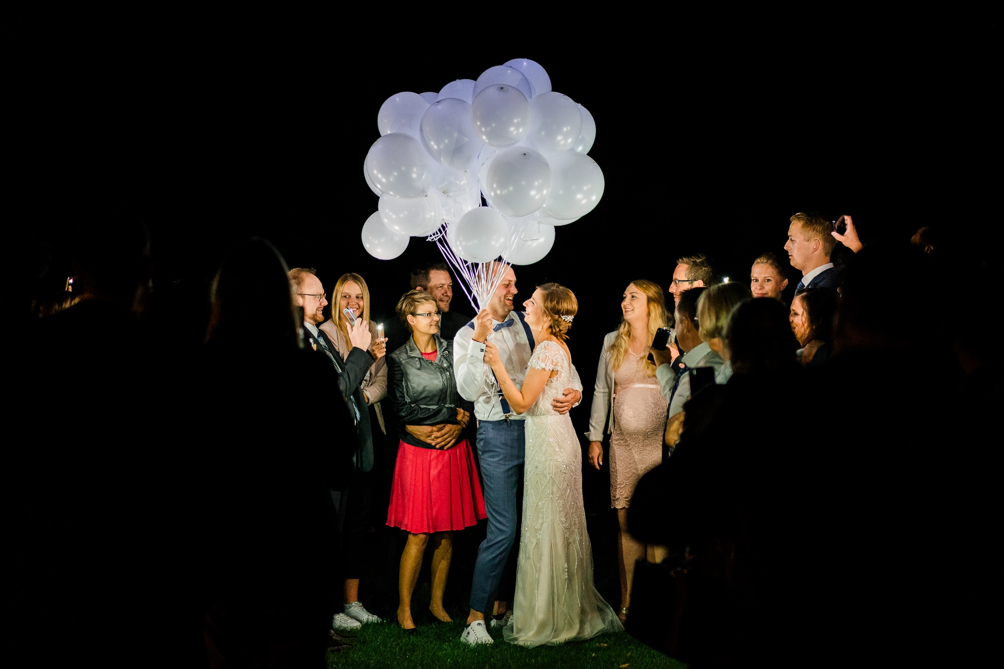 Brautpaar hält nachts weiße Luftballons fest bei einer Hochzeit in Rheine umringt von Hochzeitsgästen
