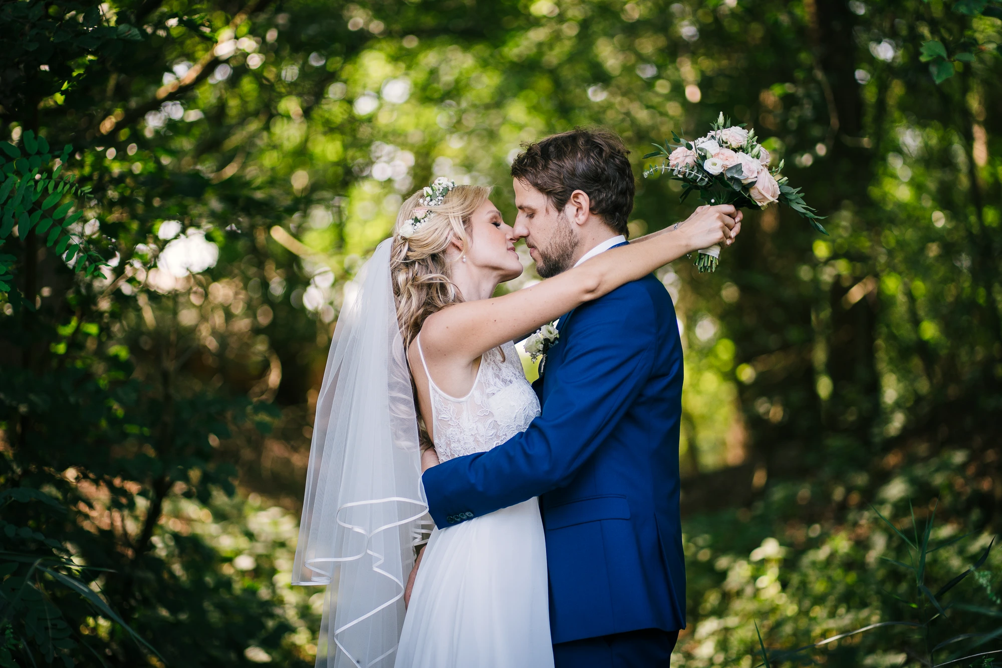 Brautpaar küsst sich in einem sonnendurchfluteten Wald an ihrem Hochzeitstag in Rheine