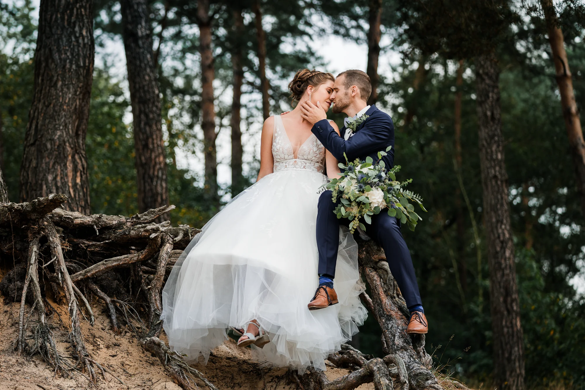 Brautpaar sitzt auf einem Baumwurzeln im Wald an ihrem Hochzeitstag