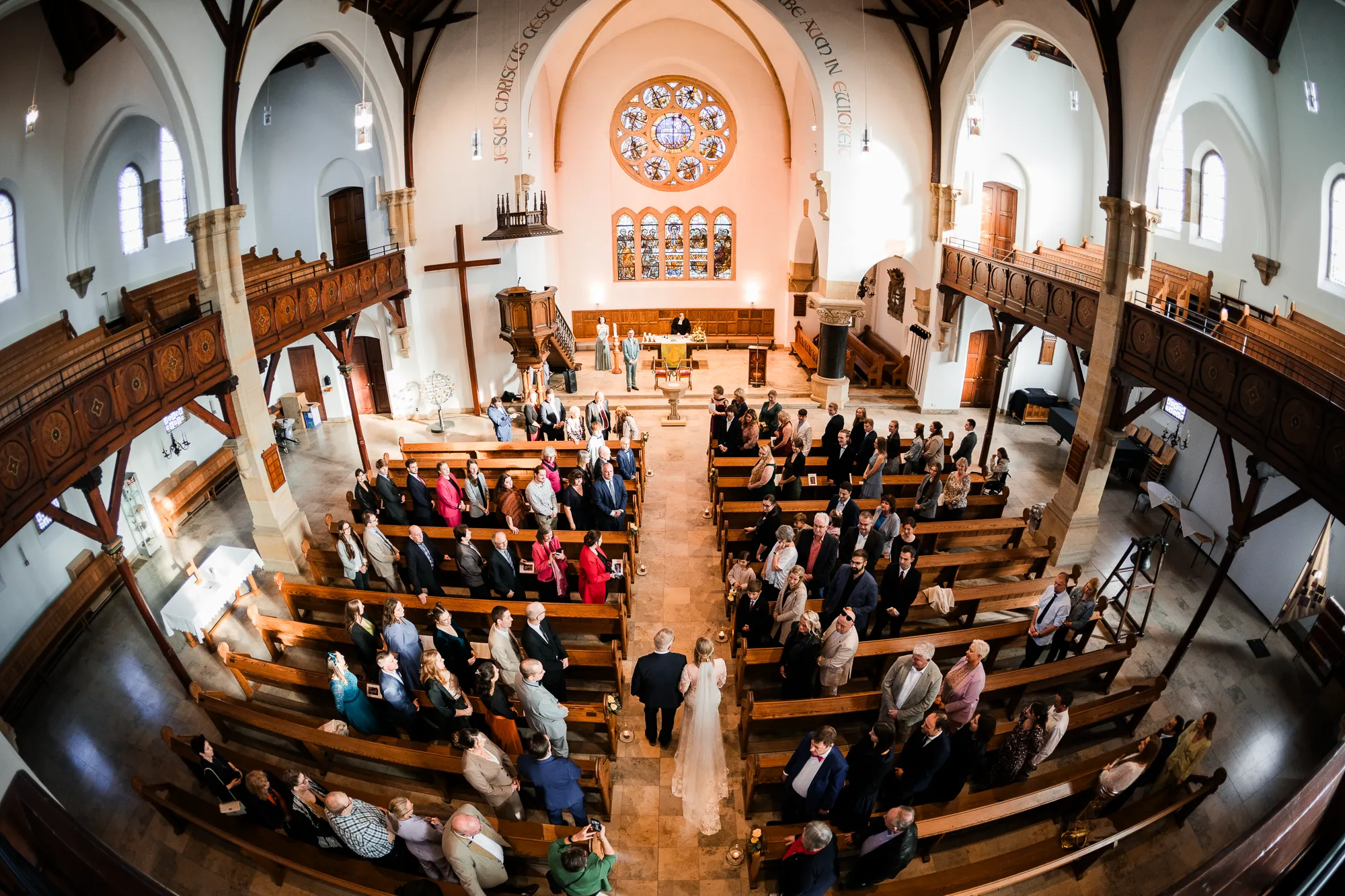 Blick von oben auf den Einzug der Braut mit ihrem Vater durch das Mittelschiff der vollbesetzten Kirche bei einer Hochzeit in Rheine