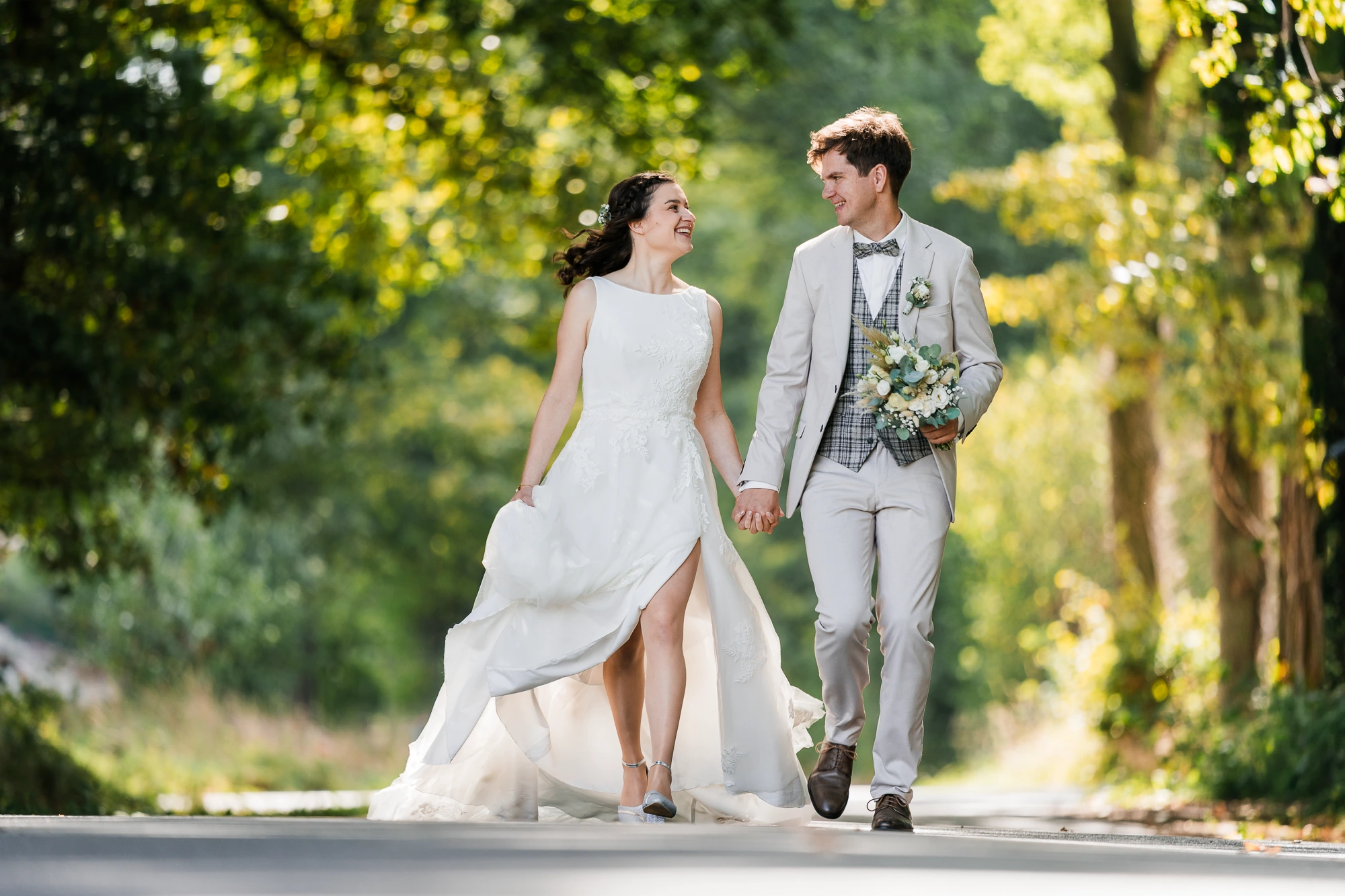 Brautpaar läuft Hand in Hand eine Allee entlang und lacht sich dabei an – Hochzeitsfotograf Rheine two4memories